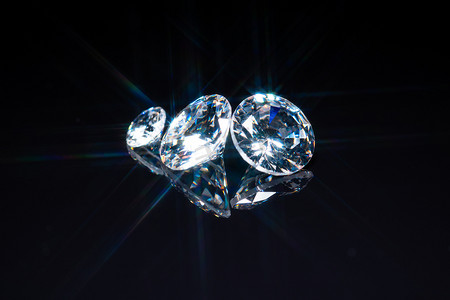 珠宝宝石摄影照片_钻石对黑色反光背景的选择性聚焦。不同尺寸的抛光宝石切割。光反射为星形射线暴、星暴或太阳光。优质珠宝展览.