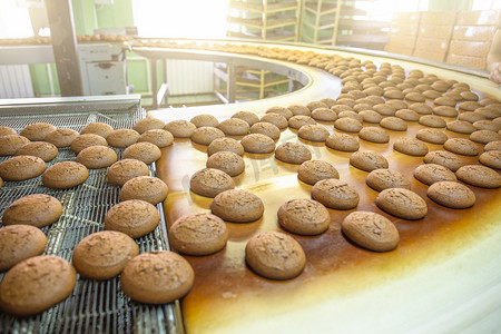 儿童烘焙手绘海报摄影照片_烘焙生产线或传送带上有新鲜的甜饼干。糖果厂车间、工业食品生产设备机械.
