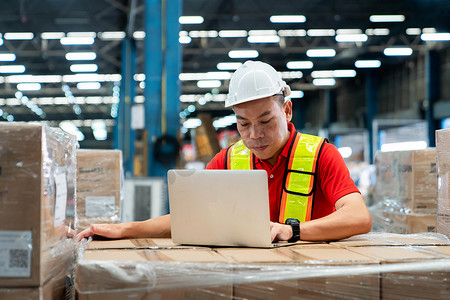 senior摄影照片_Senior male engineer looking product number of spare part in his hand for checking inventory stock in laptop at warehouse office