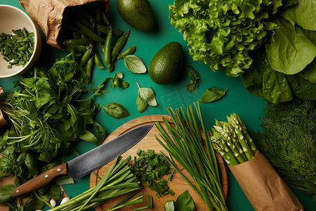 木制切板和刀在绿色表面的各种熟蔬菜的顶部视图