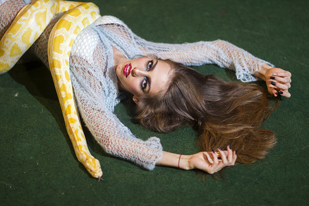 性感女人用白化蟒蛇放松。蛇在长头发的女人身上爬行。化妆脸和黄色蛇的美容模型。危险诱惑和欲望概念.