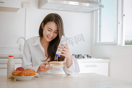 挤牛奶摄影照片_早上，女人把甜的浓缩牛奶挤成面包。桌上有牛奶、水果和苹果。