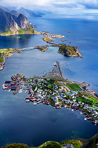 从Reinebringen山脊俯瞰挪威Lofoten岛上令人震惊的高山和Reine村的阳光鸟瞰全景。有彩虹和崎岖山峰的风景美景.