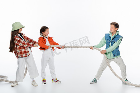 side view of cheerful girls pulling rope while playing tug of war game with boy on white