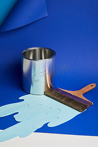 刷子油漆摄影照片_金属光泽罐，刷子和滴纸油漆在明亮的蓝色背景