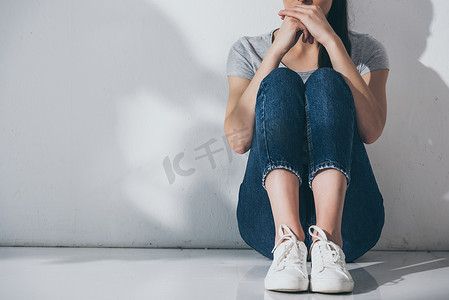 在灰色墙边坐在地板上的忧郁的年轻女子的裁剪镜头