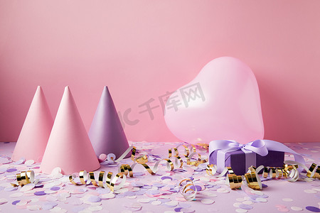 紫色桌面摄影照片_心形气球, 派对帽和紫色桌面上的礼物