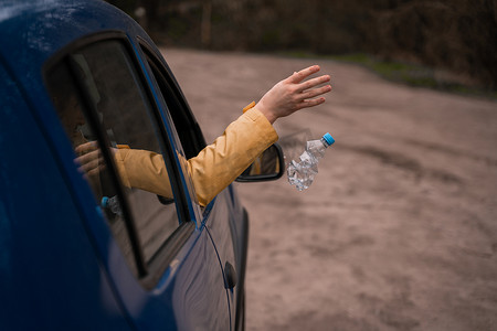 人从车上扔掉空塑料瓶的剪影