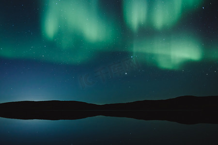 在湖面附近的夜空中, 与平静的水, 绿色的北极光和星星的简约景观。俄罗斯摩尔曼斯克地区