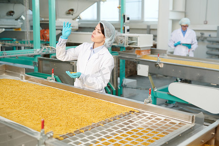 在现代食品厂工作的年轻女子的肖像，并在生产线上检查通心粉，复制空间