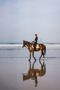 年轻女子骑马骑马在海滩附近的沙滩上