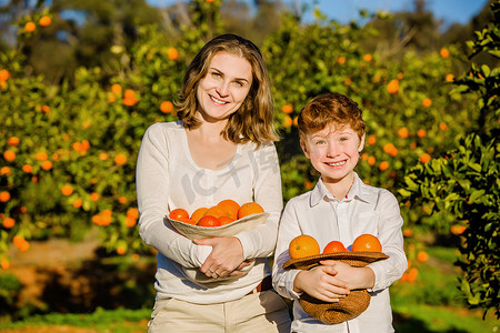 Smiling happy mother and son hold oranges in their hats on citrus farm 