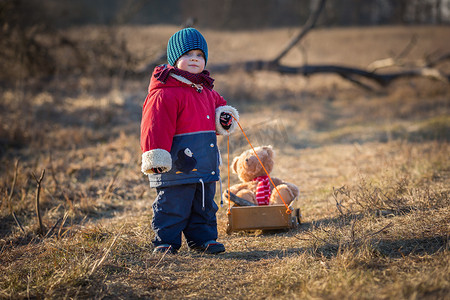 年轻快乐的男孩玩户外与他的玩具熊和小车