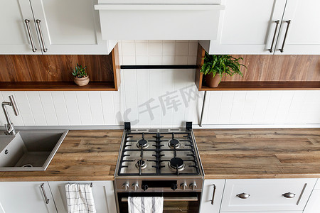 灰色橱柜摄影照片_时尚的浅灰色厨房内饰与现代橱柜和不锈钢家电在新家。斯堪的纳维亚风格的设计。绿色植物装饰, 木台面, 水槽和火炉