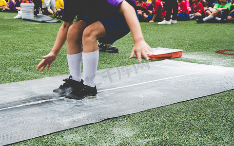 在学校体育竞赛日，学生们在橡胶板上跳远、滑脱或沙坑。 学校体育日跳远比赛(专注于脚)).