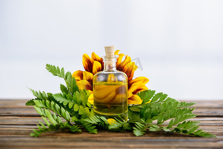 精油熬制摄影照片_木质表面用精油、植物叶和向日葵塞装的瓶子