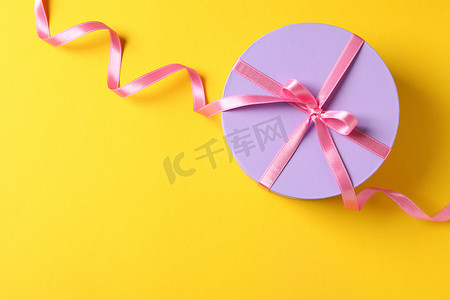 Round gift box with bow on yellow background