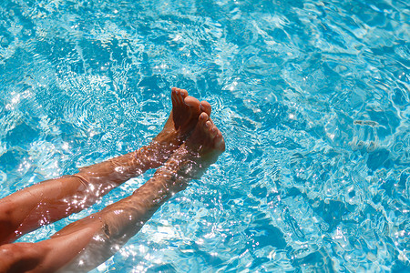 蓝色的水中的女性脚。水池里嬉戏的脚。蓝池里的水是从女性腿部的水花。妇女的腿玩在泳池里的水。游泳池中嬉戏的女人.