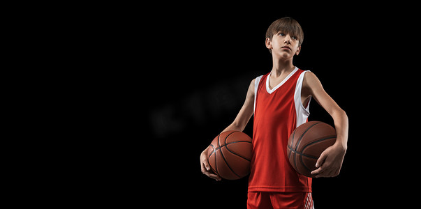 剪下小男孩的肖像，身穿红色制服的篮球运动员站在那里，在黑色背景下与球隔离。Fley