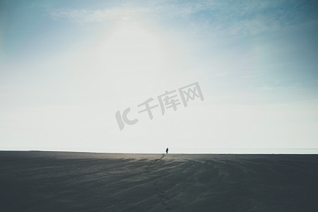 走到摄影照片_男子独自走到地平线在冰岛的黑色沙滩上留下脚印