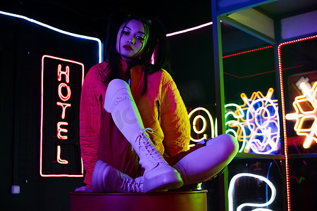 young asian woman sitting near neon sign with hotel lettering outside 