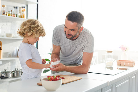 微笑的父亲帮助儿子擦手用餐巾在桌附近与草莓在厨房里 
