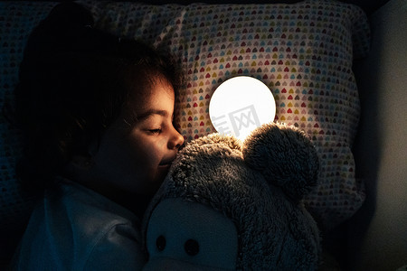 2岁的女孩躺在房间的黑暗中，点着一盏小灯，想睡着.