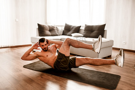 年轻人在家里参加体育活动.照片上的裸男运动员在瑜伽垫上做腹肌运动。训练新生热身。一个人在阳光灿烂的公寓里伸懒腰