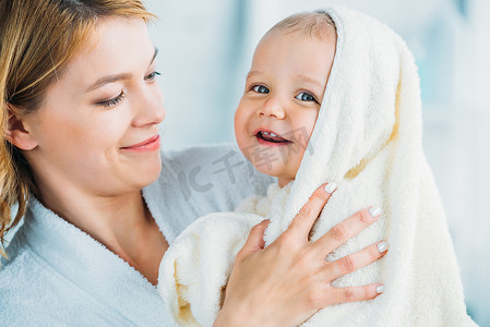 微笑的母亲在浴袍抱着快乐的小孩裹着毛巾