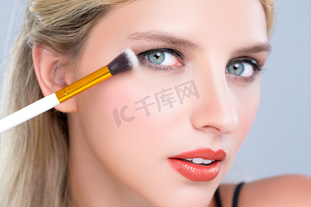 Closeup beautiful girl with flawless applying alluring eye shadow makeup with eyeliner brush. Cosmetic facial painting process on lovely young woman with perfect clean skin on isolated background.