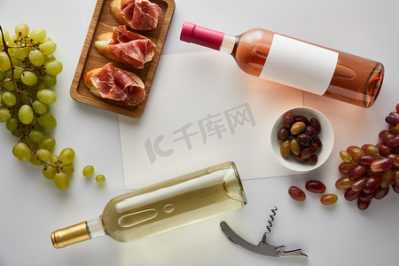 葡萄酒、软木塞、空白纸、橄榄和切碎的意大利煎饼、白底面包等附近的白葡萄酒和玫瑰酒的顶部视图