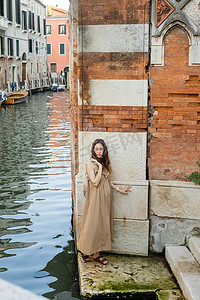 Pregnant woman in dress holding string bag near river and building in Venice 