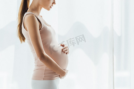 捂肚子女摄影照片_孕妇在家中摸肚子的剪影