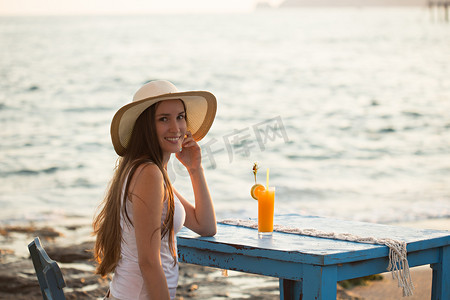 美丽的年轻女子坐在咖啡馆海边与橙色瑞