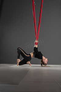 飞瑜伽。年轻女子练习空中反重力瑜伽与吊床在健身俱乐部的灰色背景.