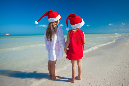 Back view of Little cute girls in Christmas hats on the exotic beach
