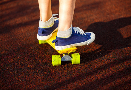 穿着蓝色运动鞋骑在活动的黄色滑板上,紧紧抓住腿. 积极的城市青年生活方式、培训、业余爱好、活动理念. 积极的儿童户外运动。 儿童滑板.
