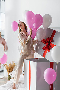 在卧室的生日派对上，年轻的女人带着节日气球打开巨大的礼物 