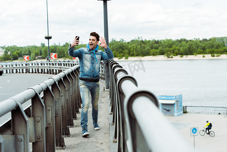 轻松愉快的男人在桥上走路时用智能手机进行视频通话的选择性焦点 