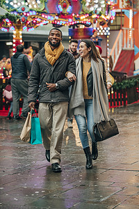 一对幸福的情侣走在城市街道的前视图。在他们身后是一个有趣的公平骑。这对夫妇正在搬运购物袋。.