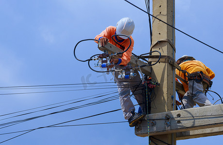 2名配有安全设备的电工正在蓝天背景下的电线杆上安装电力系统