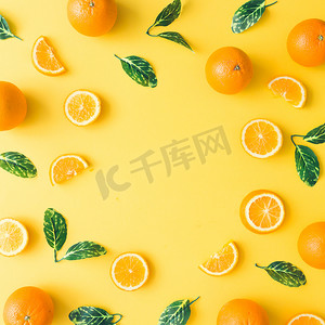 夏日图案摄影照片_在柔和的黄色背景下, 用橘子和绿叶制作的创意夏日图案。水果最小的概念。平躺.