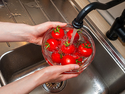 一个女人的手在自来水里放着西红柿，在鳕鱼大流行期间，处理和彻底清洗蔬菜和水果的重要性