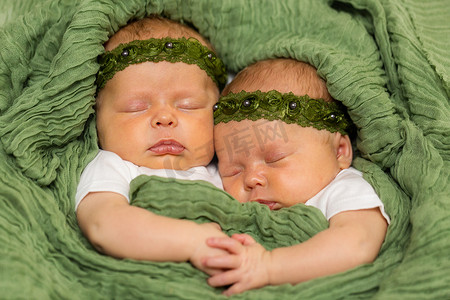 双胞胎婴儿摄影照片_两个相同的双胞胎婴儿女孩身穿绿色头巾依偎在一起的毯子牵手
