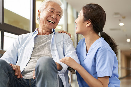 nursing摄影照片_young friendly asian female caregiver talking to elderly man in 