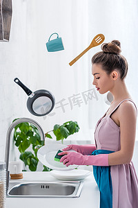 年轻女子在橡胶手套洗碗, 而炊具悬浮在空气中 