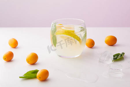 杯柠檬水, 薄荷叶和柠檬片包围冰块, 金橘紫色背景 