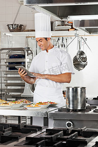 快乐的厨师在厨房中使用数字平板电脑