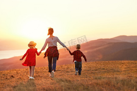Back view of happy family: mother and two kids boy and  girl running outdoors  on sunset