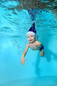 婴孩在圣诞老人的帽子, 用蓝色眼睛, 游泳在水下在一个蓝色背景水池。肖像.在水下射击。垂直方向